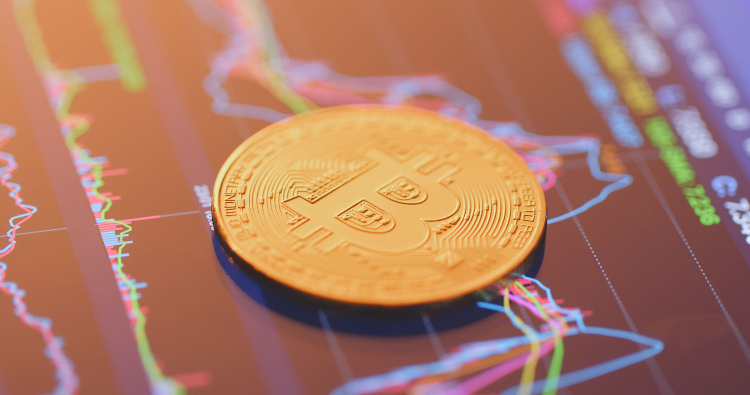 Coin representing bitcoin next to a graphic showing the cryptocurrency's price variation